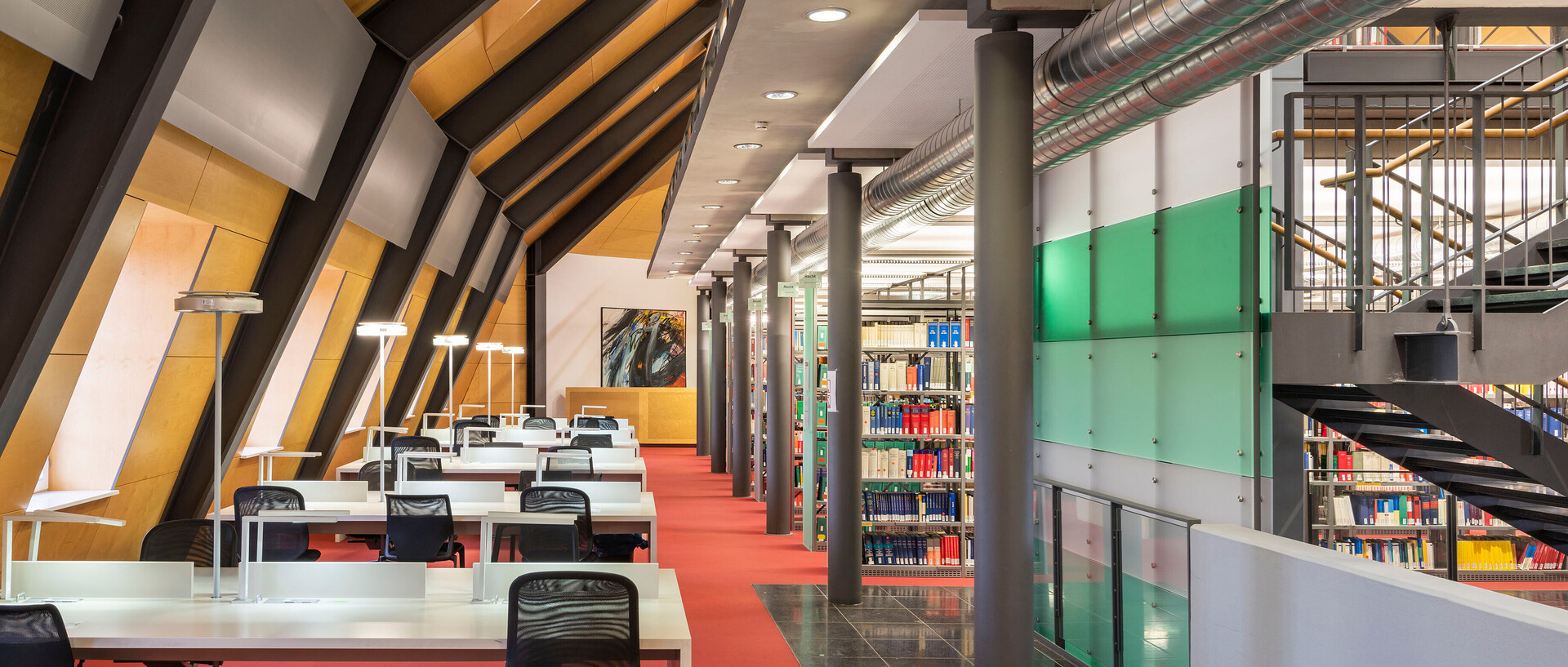 Dachgeschoss im Bibliotheksbereich Schloss Ehrenhof mit Schreibtischarbeitsplätzen Bücherregalen und Treppenaufgang.